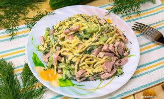 Готовый салат с яичными блинчиками и колбасой в тарелке, украшенный зеленью.