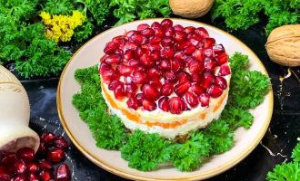Готовый мясной салат с гранатом и грецким орехом, подача на тарелке.