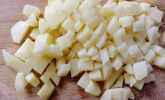 Нарезанный кубиками картофель на разделочной доске
