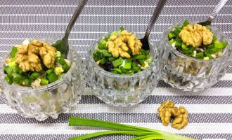 Салат с курицей, черносливом, грецким орехом и свежим огурцом, поданный порционно в креманках и украшенный зелёным луком и половинками орехов.
