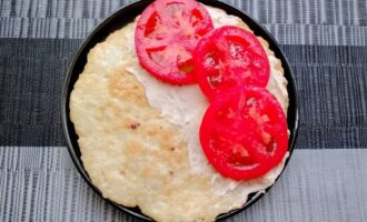 Готовый куриный блинчик, смазанный творожным сыром и уложенными ломтиками помидора.