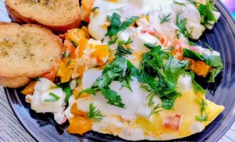 Яичница с брынзой, овощами, зеленью и чесночными гренками на тарелке