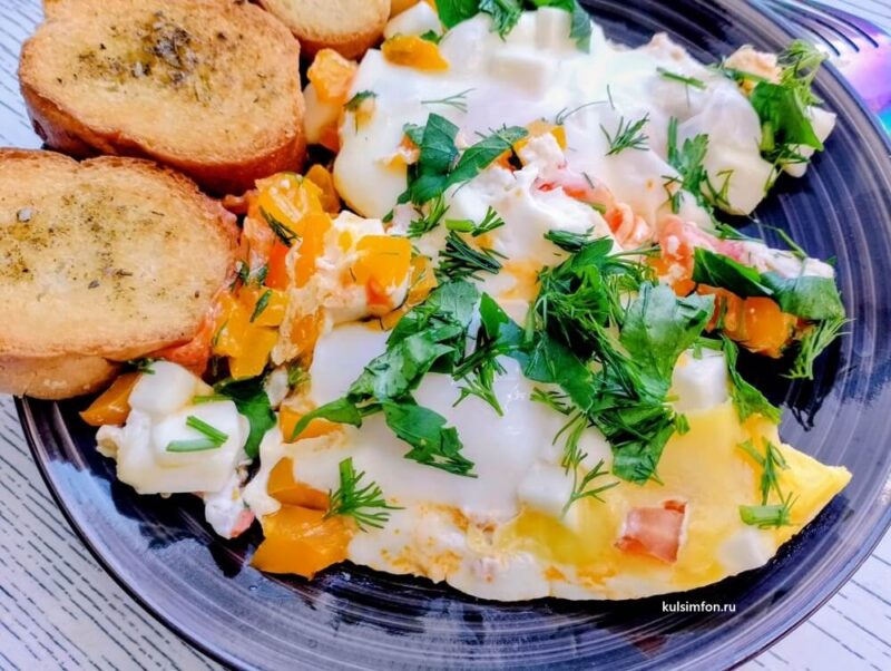 Яичница с брынзой, овощами, зеленью и чесночными гренками на тарелке